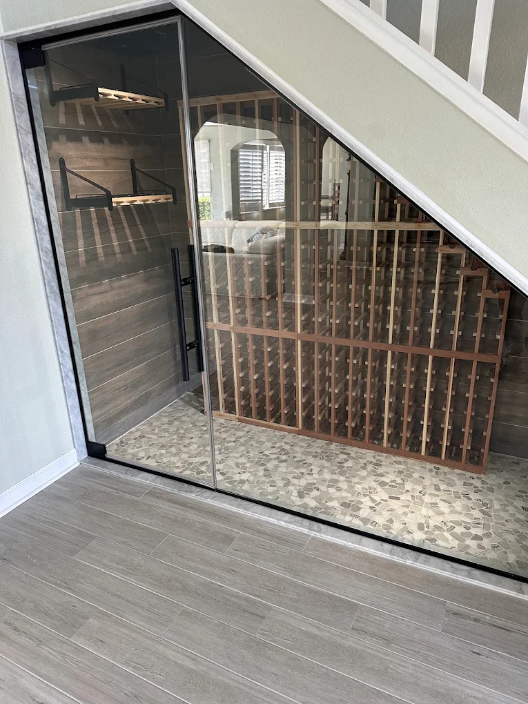 Custom glass-enclosed wine cellar built under a staircase with pebble tile floor